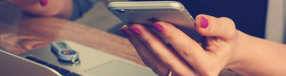 Woman holding a phone over a laptop. Photo: Firmbee.com on Unsplash.