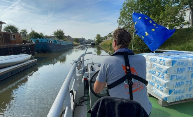 Man steering a barge with an EU flag waving.