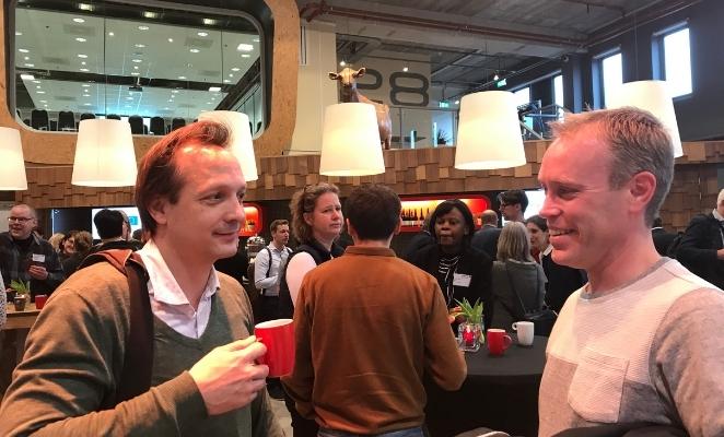 Two men in onversation at a North Sea implementation seminar, holding coffee cups in a lobby.