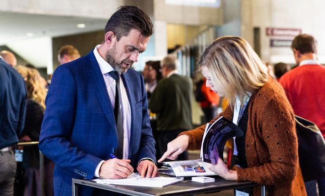 Businessman and businesswoman looking at documents together in a lobby filled with people.