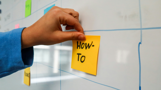 A post-it on a whiteboard with the text How To. Photo: Walls.io on Unsplash