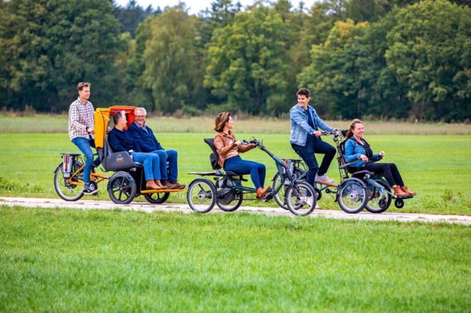 A group of six people cycle in a park using different kinds of adapted vehicles