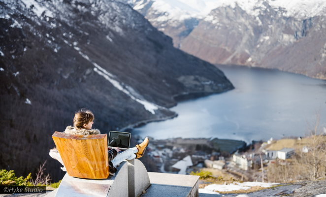 Lady seated in an armchair at the top of a mountain overlooking a gorgous Norwegian fjord. 