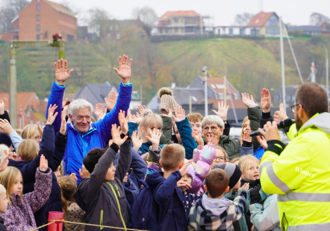 A large group of people standing outdoors, raising their hands.