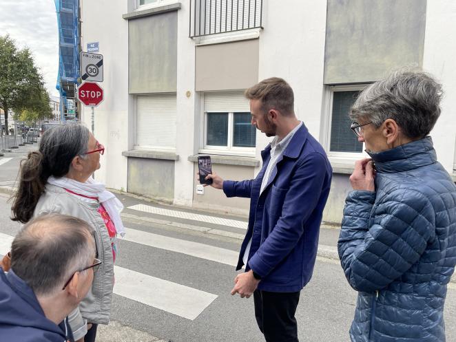 Four people are standing next to a pedrestrian crossing. One of them, a man, is showing the screen of his phone while he uses the app