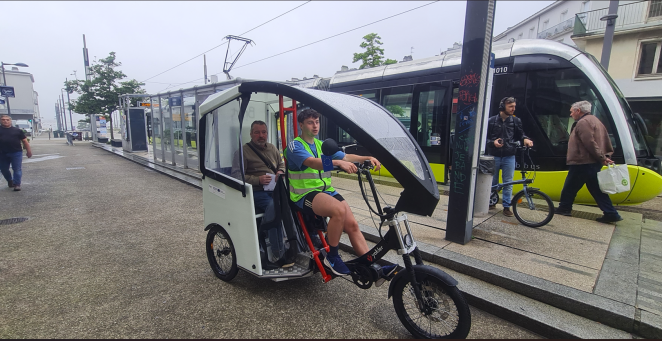 Nicholas Hastings is shown operating an electric rickshaw. A passenger is seated in the back
