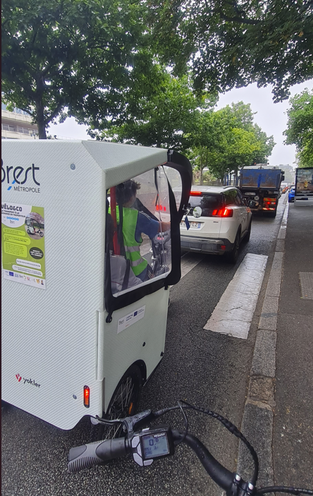 The rickshaw is photographed from the back. Nicholas is driving it in Brest's traffic