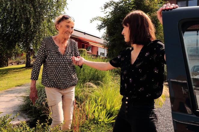 Two women are visible in the picture. The younger one is holding the hand of the older one, in order to help her get in a car