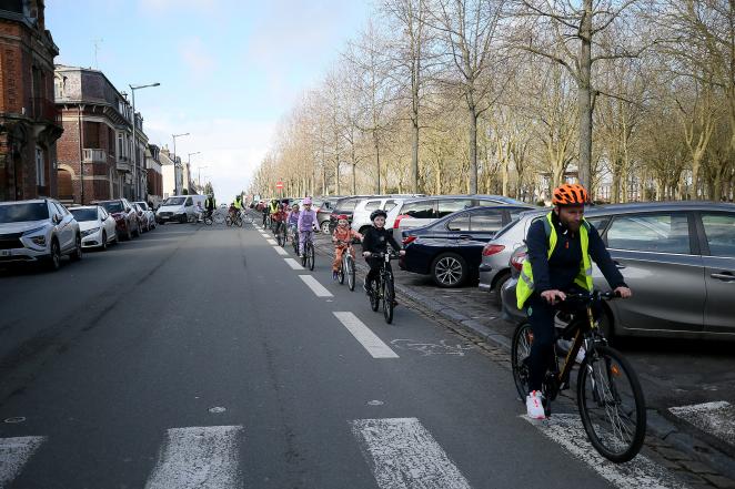 Children ride bikes on a bike lane. They're in an orderly line. An operator opens the line and guides them.