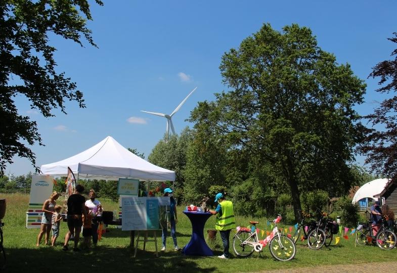 Tent and people in a green open space on a sunny day, with wind turbines.