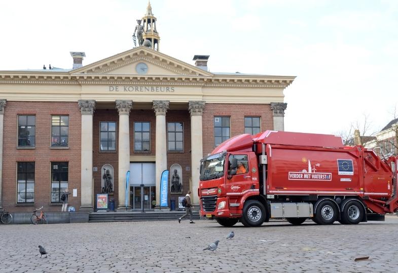 Large red hydrogen-fuelled garbage truck with a large EU flag painted on it parked in a city square.