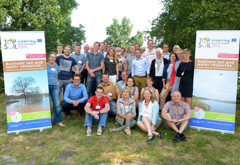 The TOPSOIL team gathered outdoors next to two roll-ups, with trees in the background