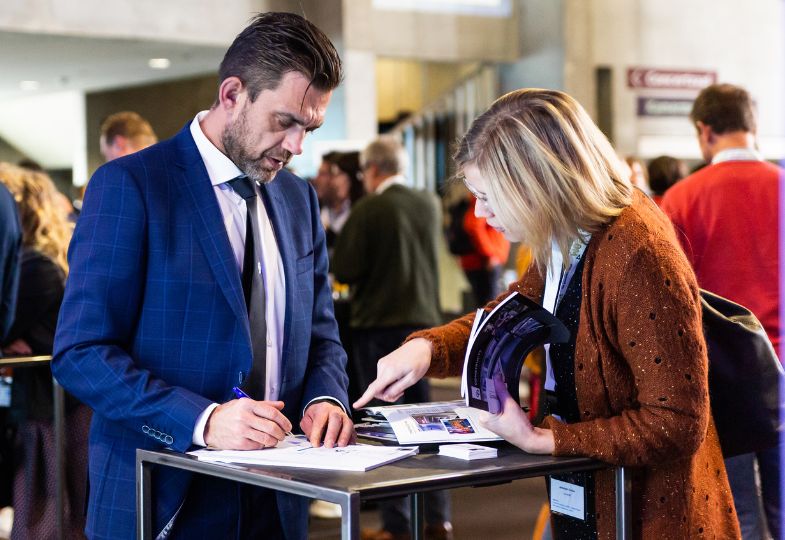 A man and a woman standing at a conference lobby table, looking at documents together