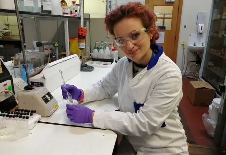 A young lady wearing protective glasses, a white lab coat and violet gloves working in a laboratory