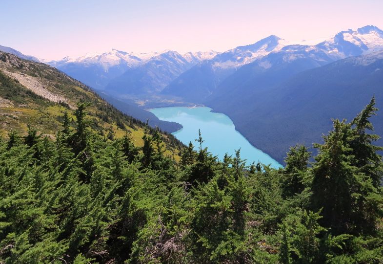 A mountainous landscape with steep mountains, snowcapped mountain peaks, and a blue lake