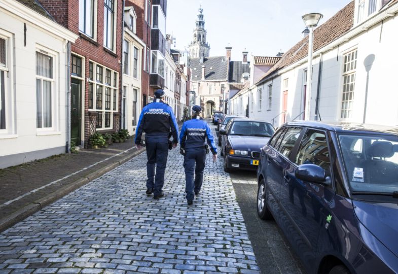 Two police officers in uniform walking down a quiet city road with cobblestones
