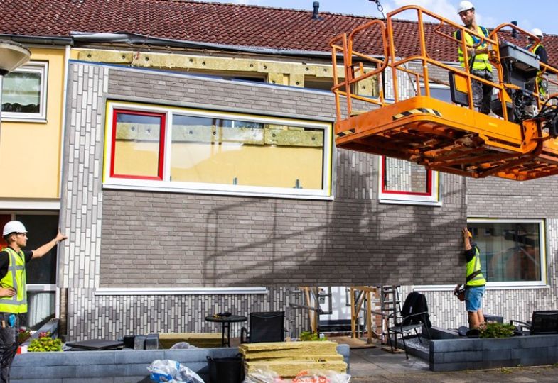 Two construction workers in an orange lift in front of retrofit cladding that is being put into place