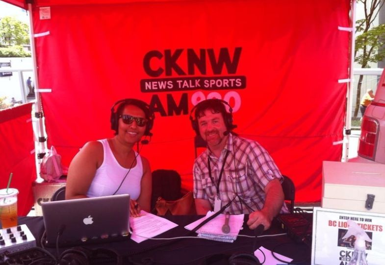 Two smiling journalists inside a red tent reporting from a sports event