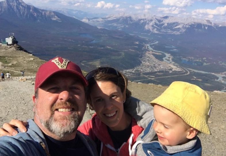 Shane Woodford with this wife and toddler in front of a mountainous landscape