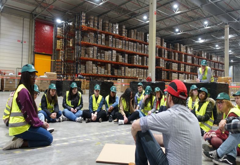 A group of young people sitting on a factory floor as part of a port introduction game, wearing helmets