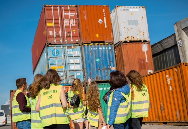 A group of people wearing yellow safety vests are inspecting containers in a harbour area.