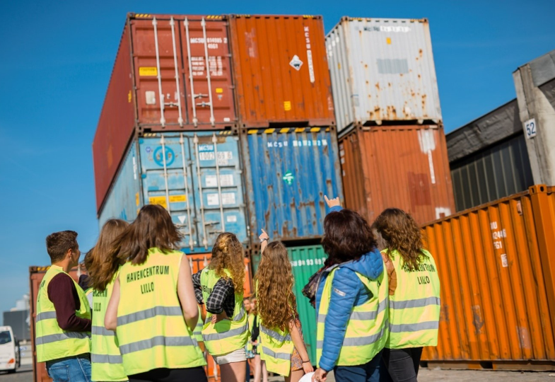 A group of people wearing yellow safety vests are inspecting containers in a harbour area. 