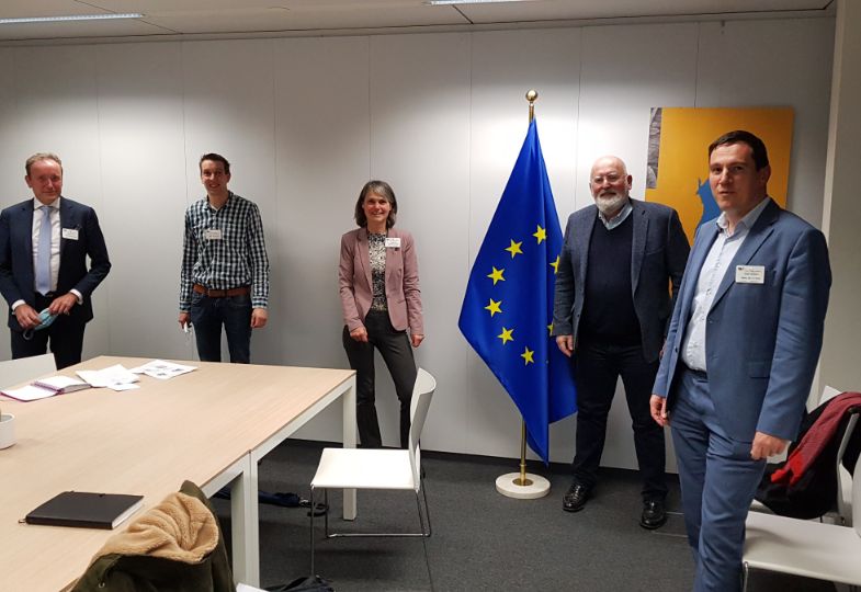 A group of people with Mr Timmermanns in his office, next to a large EU flag.