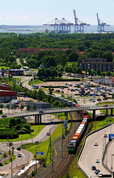 An aerial view of a green landsape with a port and sea in the background and a cargo traing in front