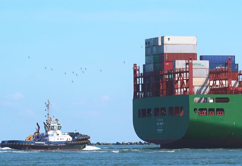 A smaller boat sailing past a huge cargo ship on a sunny day.