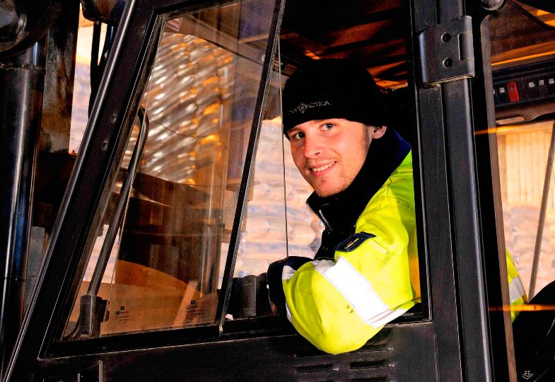 Smiling truck driver wearing a yellow safety jacket looks out from his window.