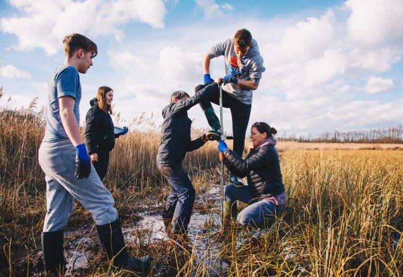 A group of three people pulling up a peat core in a large area of peatland, while two other people watch.