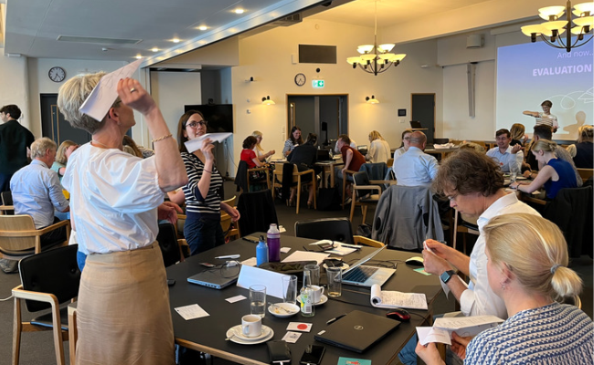 A woman throwing a paper plane in a room full of people