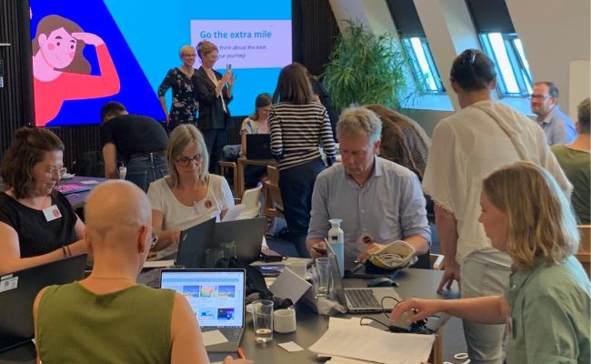 Workshop participants working at tables, with a large screen behind.