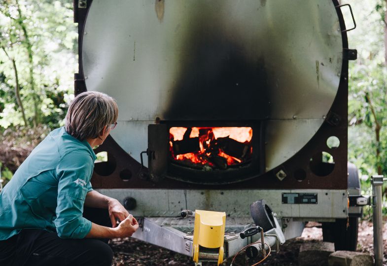 Ecologist Andrea Kelly looking into the flames of a large woodburner in the forest. 