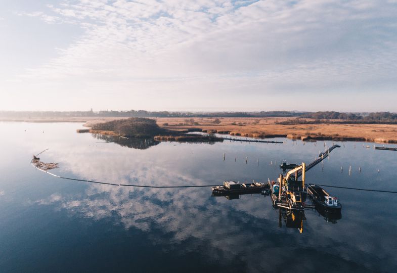 A dredging operation in a large lake surrounded by brown reeds.