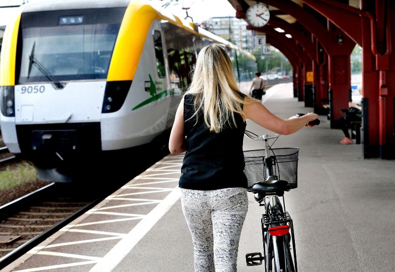 Young lady pushing a bike along a platform with a train waiting.