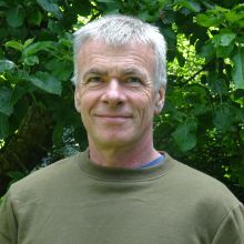 Author John Holland in front of green foliage.