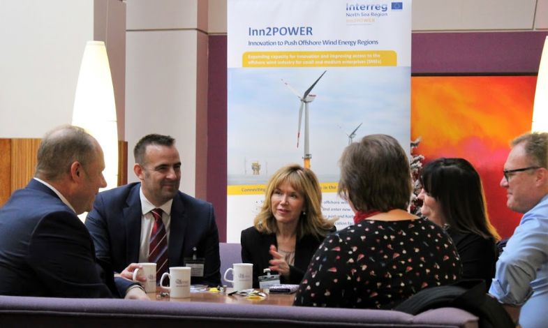 A groupo of people seated around a table in front of a roll-up displaying a wind turbine. 