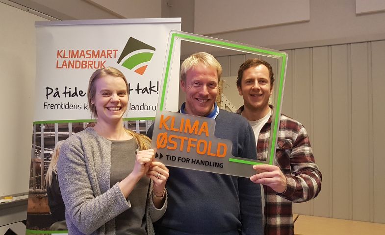 Three people holding a green picture frame saying Klima Oestfold. 