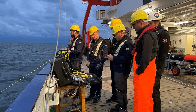 A group of workers wearing yellow helmets, on a boat in cloudy weather.