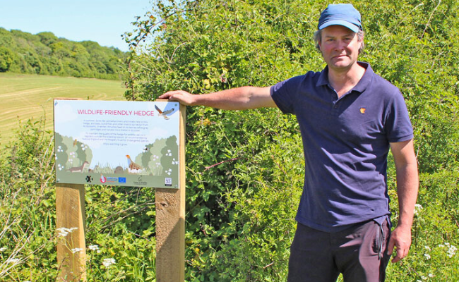 A man wearing a cap next to a signpost in the countryside.