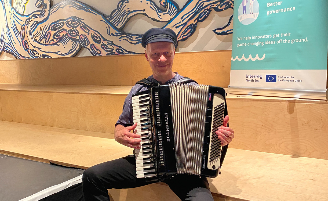 A man playing the accordion in front of an Interreg North Sea roll-up banner.