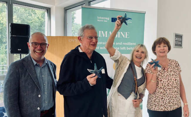 Four laughing people. Three of them hold up a blue glass starfish.