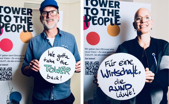 Two people holding signposts in front of posters saying "Tower to the people".