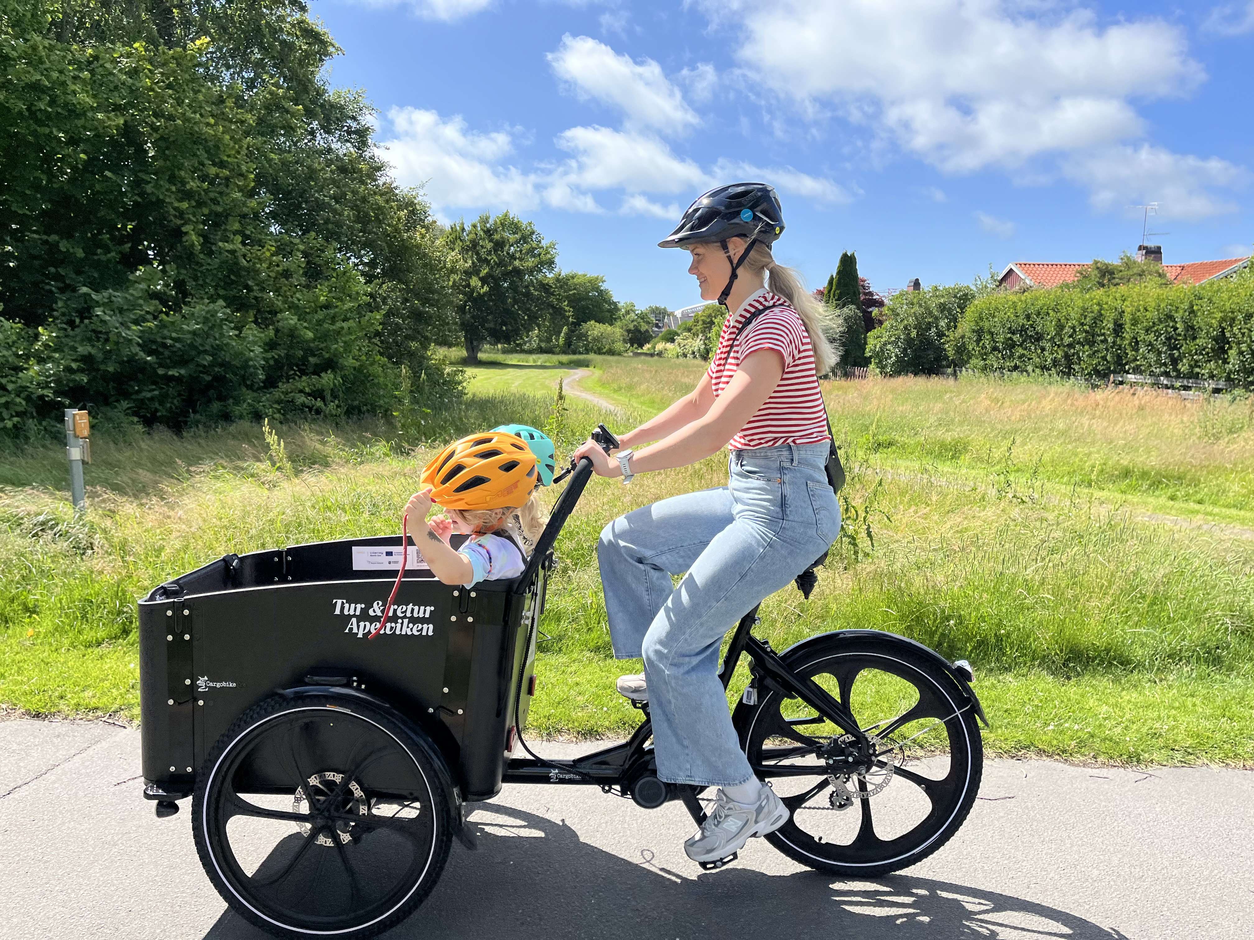 A woman drives a cargo bike. A child is in the large front basket