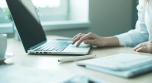 Person working with a laptop and notebook.