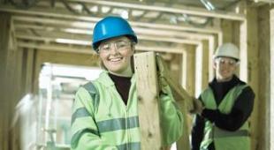 A male and female worker wearing yellow vests inside a wood construction.