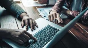 Close-up of the hands of people working together in front of a laptop.