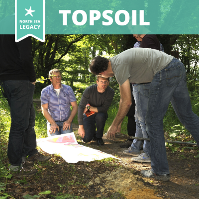 A group of people in a sunny forest studying a large map on the forest floor.