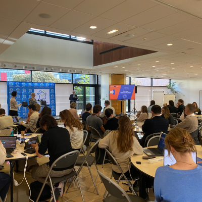 People gathered in a sunlit room, listening to a presentation.